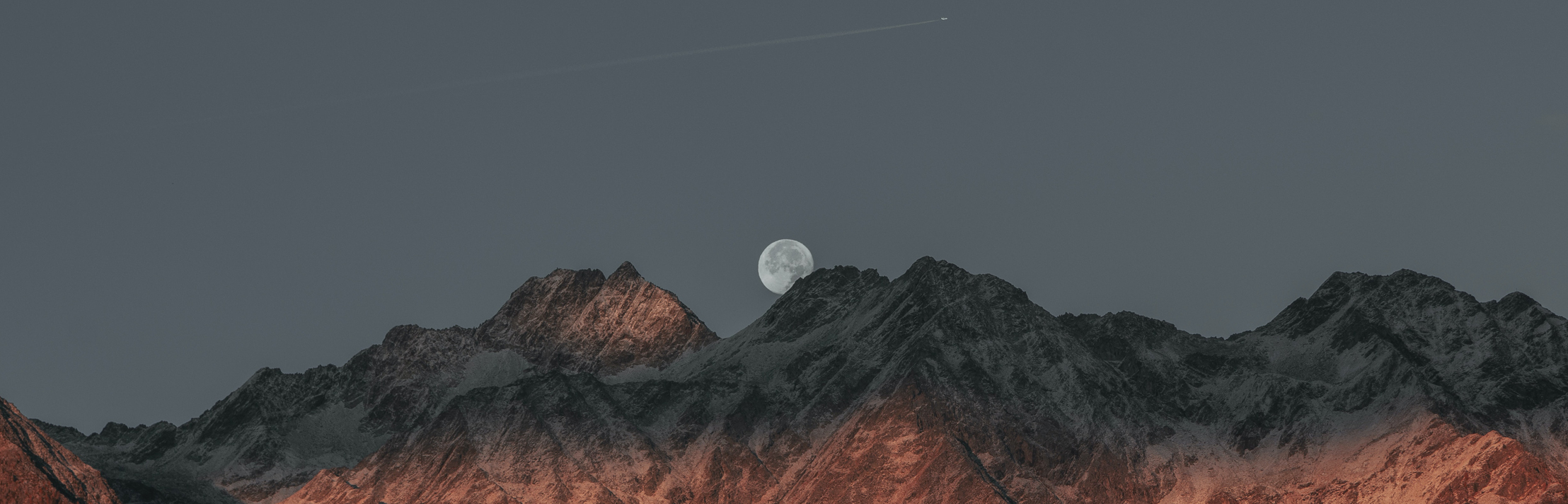 Picture of a mountain range summit with a full moon in the background